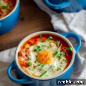 An overhead shot of three blue cocottes filled with Whole30 eggs in purgatory, baked eggs in a spicy tomato meat sauce