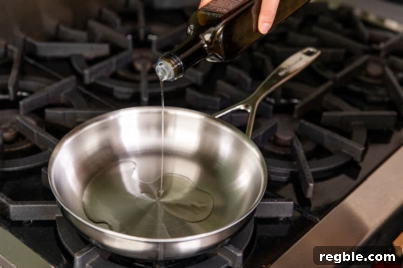 Inferno Eggs 4 An overhead shot of someone pouring extra virgin olive oil into a hot stainless steel skillet.