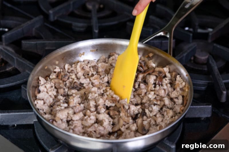 Inferno Eggs 8 A stainless steel skillet is filled with cooked Italian sausage, onions, and mushrooms.