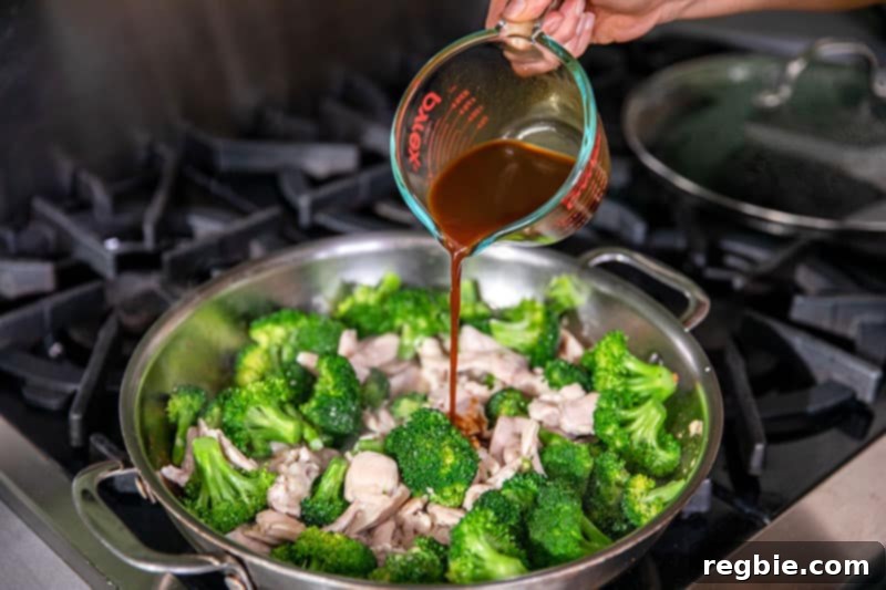 Pouring the pre-thickened All-Purpose Stir-Fry Sauce into a pan of Whole30 chicken and broccoli stir-fry, ready to create a glossy coating.
