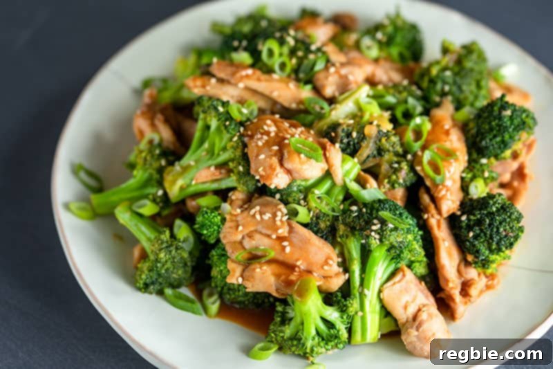 A close-up, appetizing shot of a finished chicken and broccoli stir-fry, beautifully topped with toasted sesame seeds and thinly sliced scallions, ready to be enjoyed.