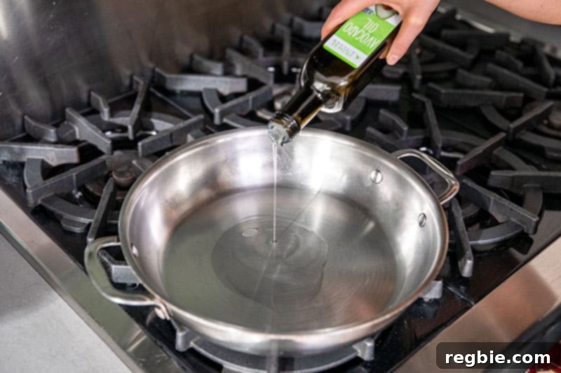 Pouring avocado oil from a bottle into a large, preheated stainless steel skillet, preparing for stir-frying.