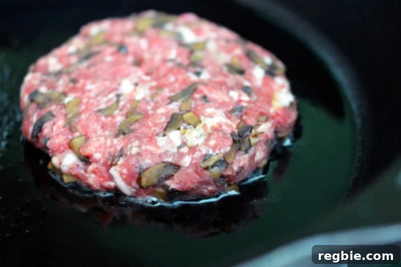 A patty of big-o bacon burger frying in a hot cast iron skillet, creating a delicious crust.