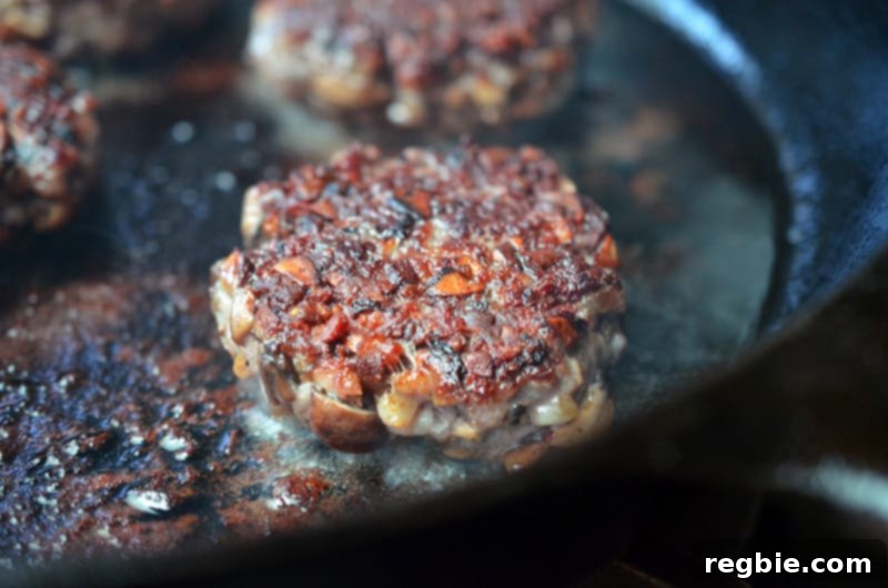 Several Big-O Bacon Burgers frying in a cast iron skillet, developing a savory crust.