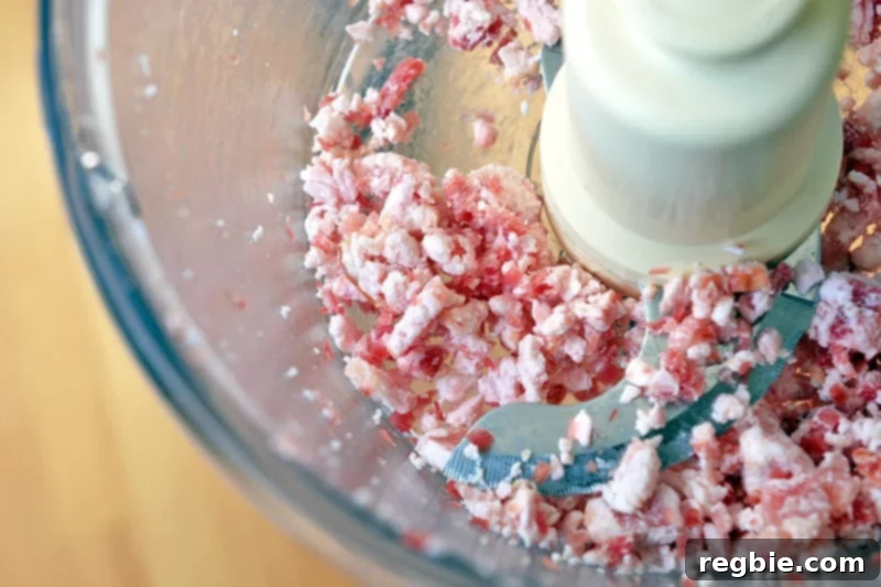 Frozen bacon being pulsed in a food processor to a ground-meat consistency.