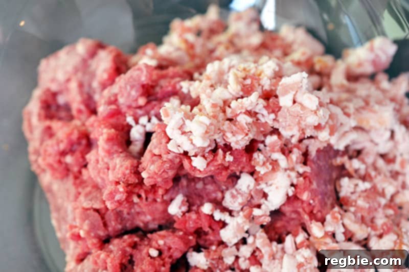 Ground beef, processed bacon, and seasonings are in a bowl, ready for mixing.