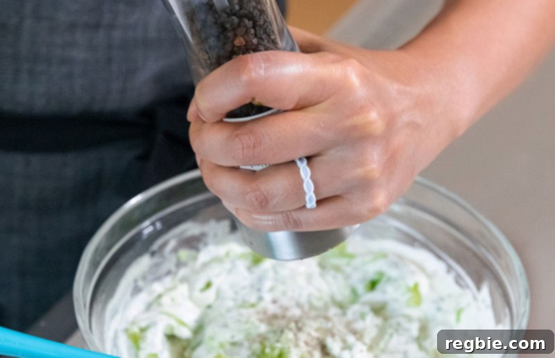 Someone adding freshly cracked pepper to a bowl of Whole30 and vegan tzatziki sauce.