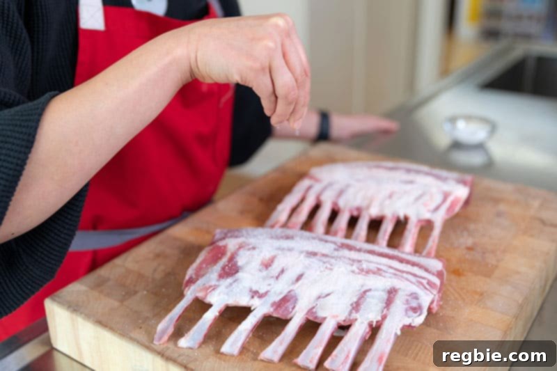 Close-up of two lamb racks being sprinkled with Diamond Crystal kosher salt, preparing them for a simple Whole30 roast.