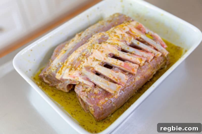 Two lamb racks submerged in a garlic lemon marinade within a white rectangular baking dish, ready for roasting.