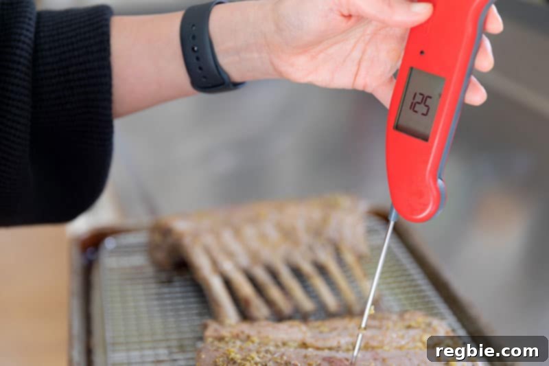 A red instant-read meat thermometer inserted into a rack of lamb displays an internal temperature of 125 degrees Fahrenheit.