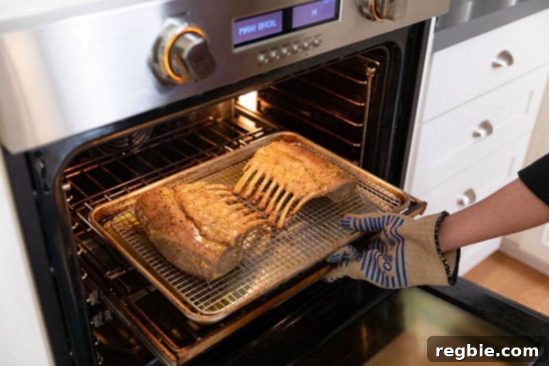 Two racks of lamb are placed back into the oven, positioned under the broiler to achieve a golden-brown crust.