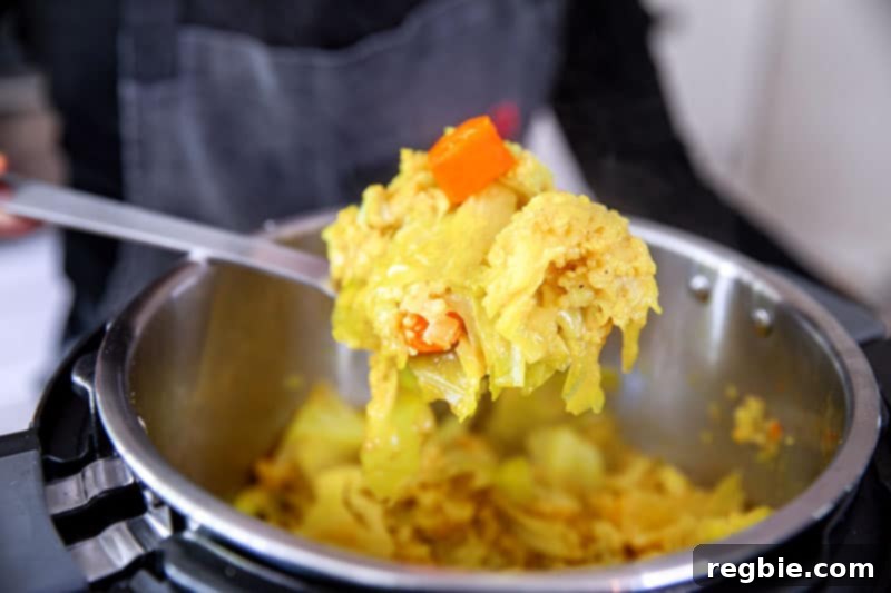 A spoonful of Instant Pot Atakilt Wat, Ethiopian cabbage stew, being scooped out of the pot, highlighting the tender vegetables and flavorful broth.