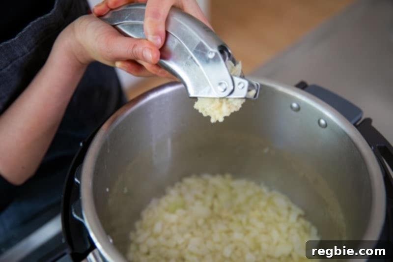 A close-up of adding freshly minced garlic to sauteed, translucent onions in an open Instant Pot, a crucial step for building the flavor base of Whole30 Atakilt Wat.