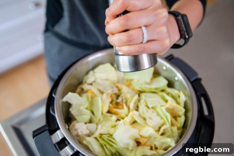 A hand sprinkles the essential spices and seasoning—turmeric, cumin, salt, and pepper—over the vegetables in the Instant Pot, preparing to infuse the Whole30 Atakilt Wat with its signature flavor.