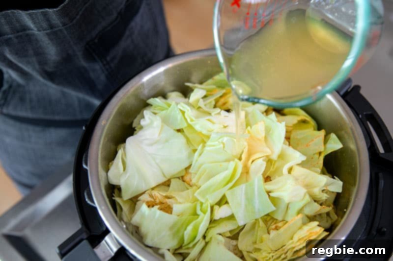 A close-up of broth being poured into an Instant Pot brimming with seasoned vegetables for Ethiopian cabbage stew, ensuring the liquid reaches the bottom for proper pressure cooking.