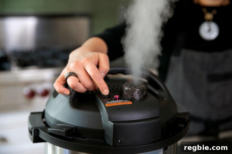 A woman's hand carefully turns the pressure release valve on an Instant Pot, with a visible plume of steam rising, indicating a manual pressure release.