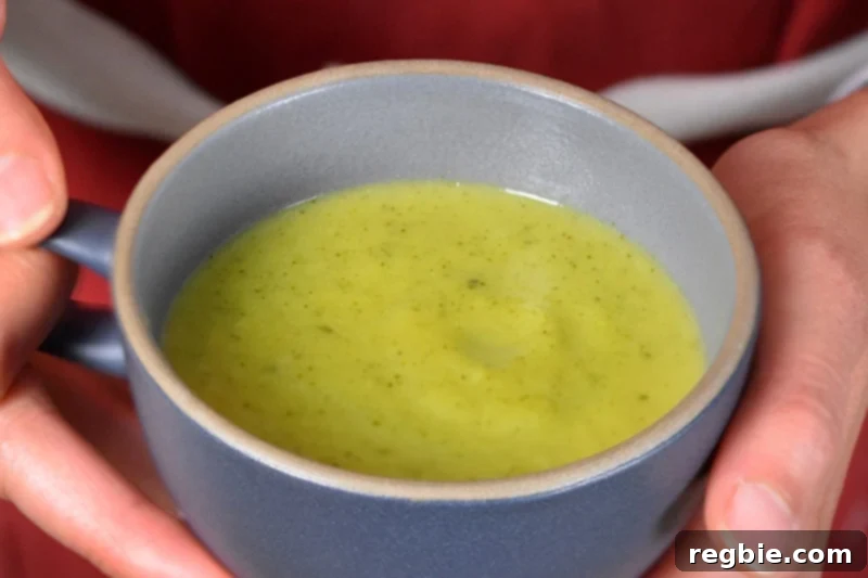 A vibrant blue coffee mug filled with creamy, paleo-friendly curried broccoli soup, garnished beautifully.