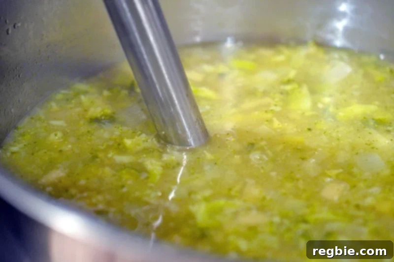 An immersion blender actively blending a pot of Whole30-compliant Curried Cream of Broccoli Soup to a smooth consistency.