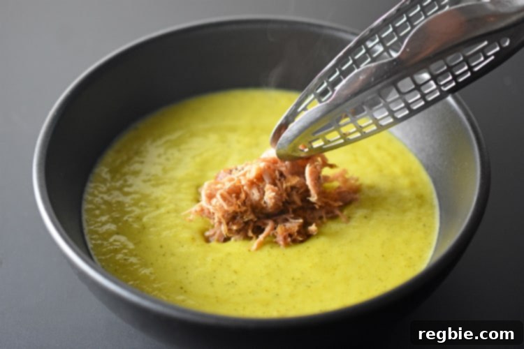 A generous serving of paleo Curried Cream of Broccoli Soup, topped with savory Kalua Pig, creating a wholesome and satisfying meal.
