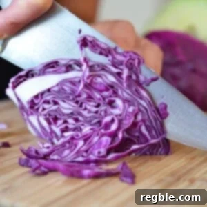 Someone slicing a red cabbage on a cutting board for paleo sautéed red cabbage with onions, garlic, and anchovy.