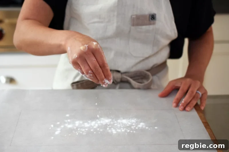 Tapioca flour being sprinkled evenly onto parchment paper, specifically over the faintly visible rectangle tracing, to prevent dough from sticking.