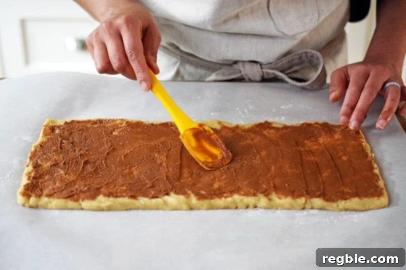 A person meticulously spreading a thin, even layer of sweet cinnamon filling over the unbaked paleo cinnamon roll dough.