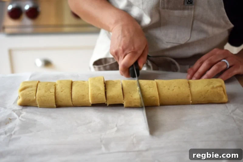 A person meticulously slicing the chilled, rolled cinnamon roll dough into twelve uniform pieces using a sharp knife.