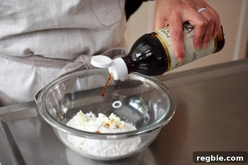 Vanilla extract being poured into a bowl containing powdered maple sugar and palm oil shortening, the base ingredients for the paleo cinnamon roll frosting.