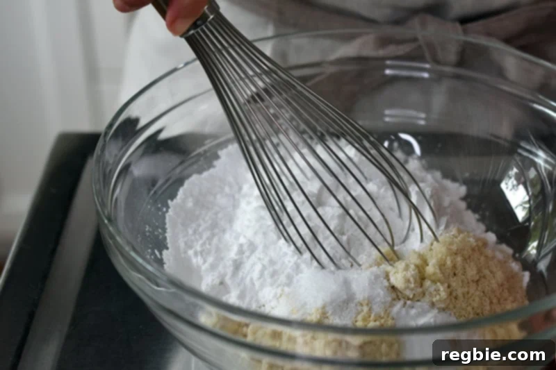 Whisking the dry ingredients for paleo cinnamon rolls including almond and tapioca flours, baking soda, and salt, in a large glass bowl.