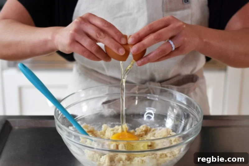 An egg being cracked into a bowl containing the semi-mixed dough for paleo and gluten-free cinnamon rolls, ready for final blending.
