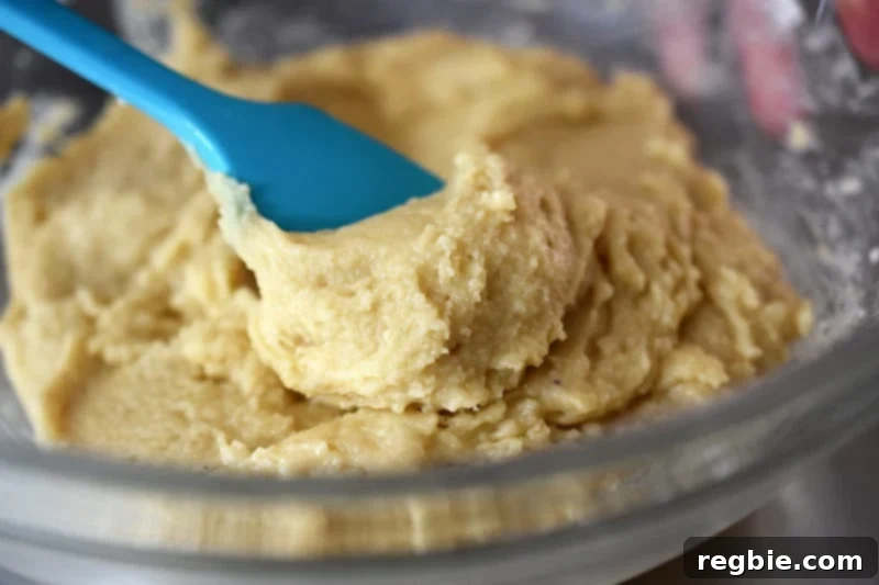 A close-up shot of the sticky paleo cinnamon roll dough being mixed with a blue silicone spatula, showing its desired consistency.