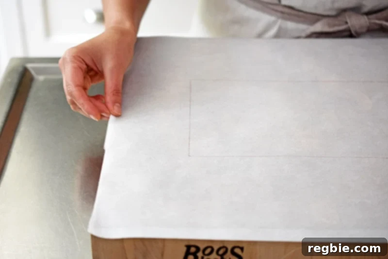 Parchment paper, with a faint rectangle tracing visible, being placed onto a wooden cutting board, ready for dough preparation.