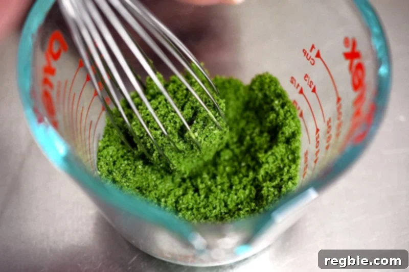 An overhead shot of a whisk combining the dry ingredients of paleo matcha mug cake in a measuring cup.