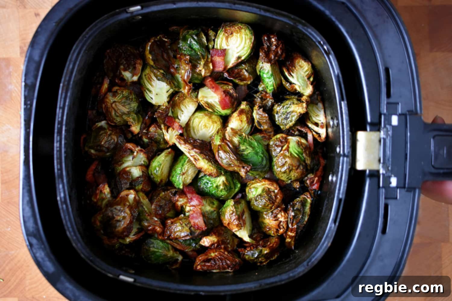 An overhead shot of an air fryer basket filled with crispy browned Brussels sprouts and bacon, fresh out of the air fryer.