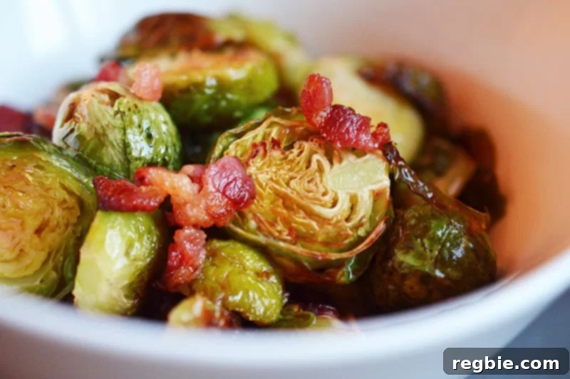 A side view of Roasted Brussels Sprouts and Bacon in a white bowl, with a balsamic glaze drizzle.