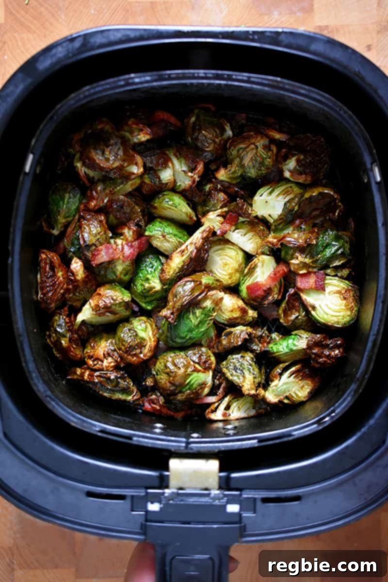 An overhead shot of an air fryer basket filled with golden brown Brussels sprouts and perfectly cooked bacon pieces.