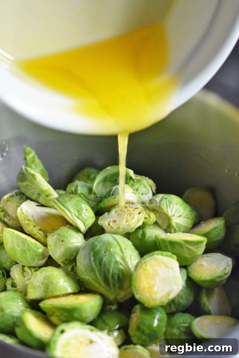 Melted ghee is poured into a bowl containing halved Brussels sprouts, ready for seasoning.