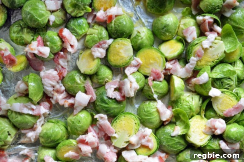 An overhead shot showing seasoned Brussels sprouts and diced bacon spread evenly on a baking tray, ready for the oven.
