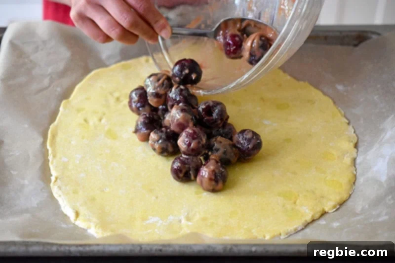 Someone spooning the cherry filling on the center of the galette dough.