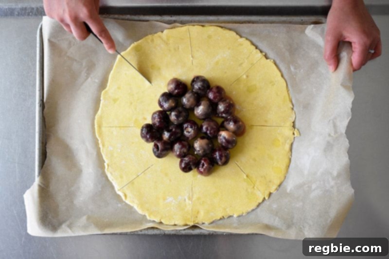 An overhead shot of someone using a paring knife to cut 8 evenly placed lines in the galette dough.