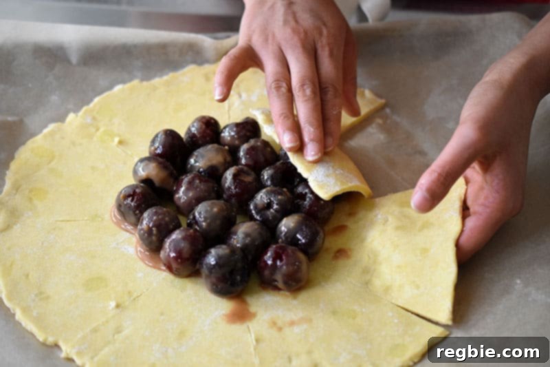 Someone folding the flaps of the galette dough over the cherry filling.