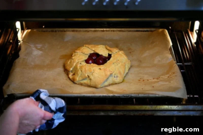 Rotating the cherry galette at the halfway baking point to ensure even browning.
