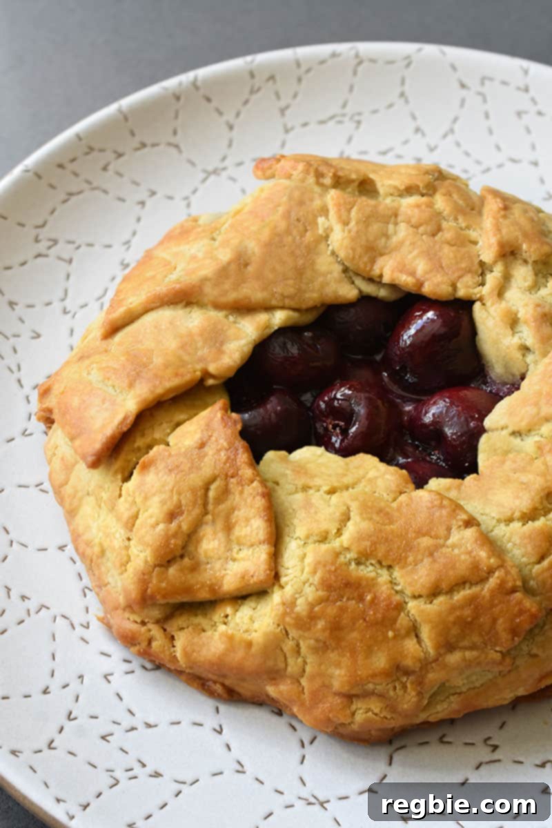 A paleo cherry galette is on a white plate ready to be sliced.