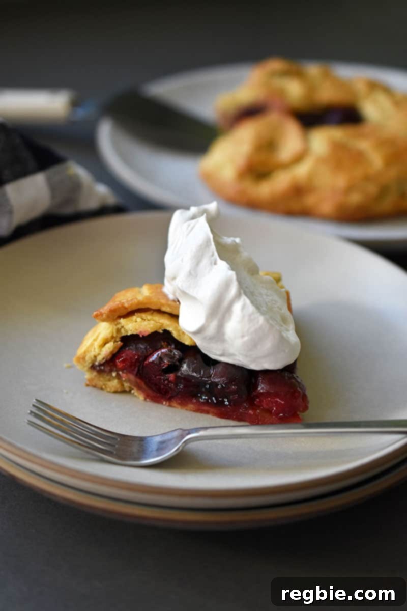 A slice of paleo cherry galette topped with whipped coconut cream is in the foreground of the picture.