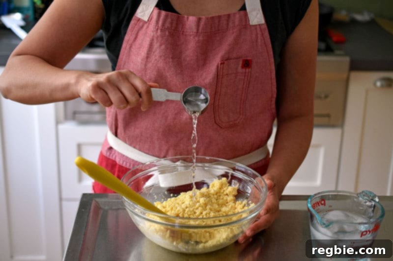 Adding a spoonful of ice water to the paleo pie dough in a bowl.