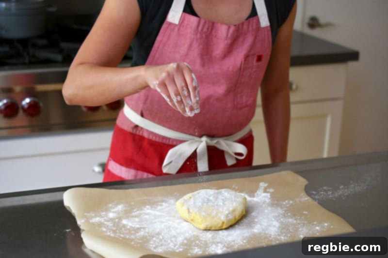 A person in a red apron is sprinkling cassava flour on top of the galette dough.