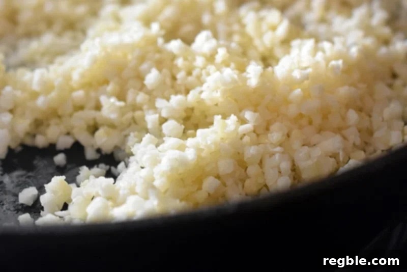 Effortless Cauliflower Rice 7 A closeup of cauliflower rice being cooked in a cast iron skillet.