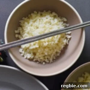 An overhead shot of cauliflower rice in a bowl topped with silver chopsticks