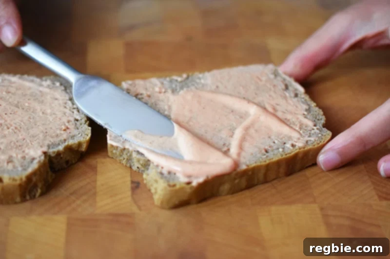A knife is spreading sriracha mayonnaise evenly on a slice of gluten-free and paleo sandwich bread.