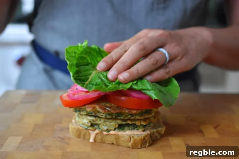 Adding a fresh piece of lettuce on top of the stacked ingredients of a paleo St. Paul sandwich.